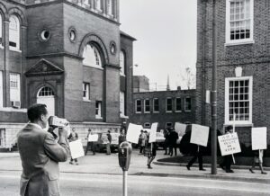 Demonstrators carrying protest signs outside a York building in the 1960s as a cameraman films